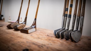 Vintage hickory golf clubs from the early 20th century displayed on a wooden workbench, showing a range of wooden-headed clubs and forged iron heads that illustrate traditional golf craftsmanship.