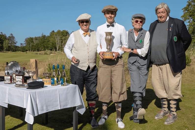 Louis Dudzus, dressed in vintage knickerbockers, white shirt, and bow tie, holding a large trophy with fellow golfers in period clothing beside him at the German Open Hickory Championship 2025.