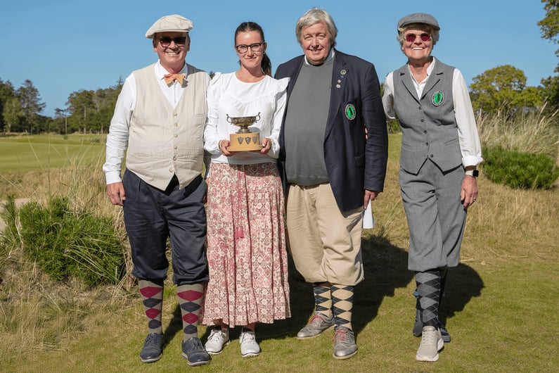 Marie Kauder, wearing a long patterned skirt and white blouse, holding a silver trophy while standing with other golfers dressed in hickory-era attire during the German Open Hickory Championship 2025