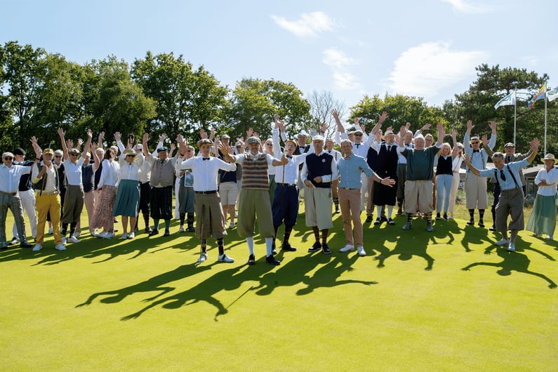 Large group photo of participants raising their arms in celebration, all dressed in hickory golf clothing, on the green during the German Open Hickory Championship 2025.