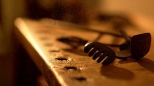 Close-up of a rare vintage golf club head, known as a rake niblick, resting on a wooden workbench in warm light.