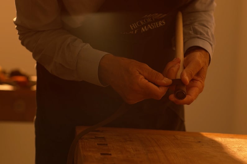 Craftsman restoring a hickory golf club by hand-wrapping the wooden shaft with new leather grip under soft sunlight.