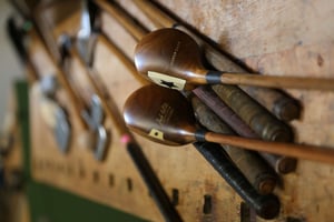 Close-up of vintage hickory golf clubs displayed on a wooden rack