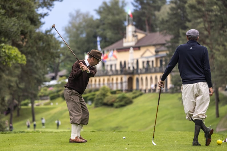 Two golfers in traditional hickory attire playing with vintage clubs on a historic golf course.
