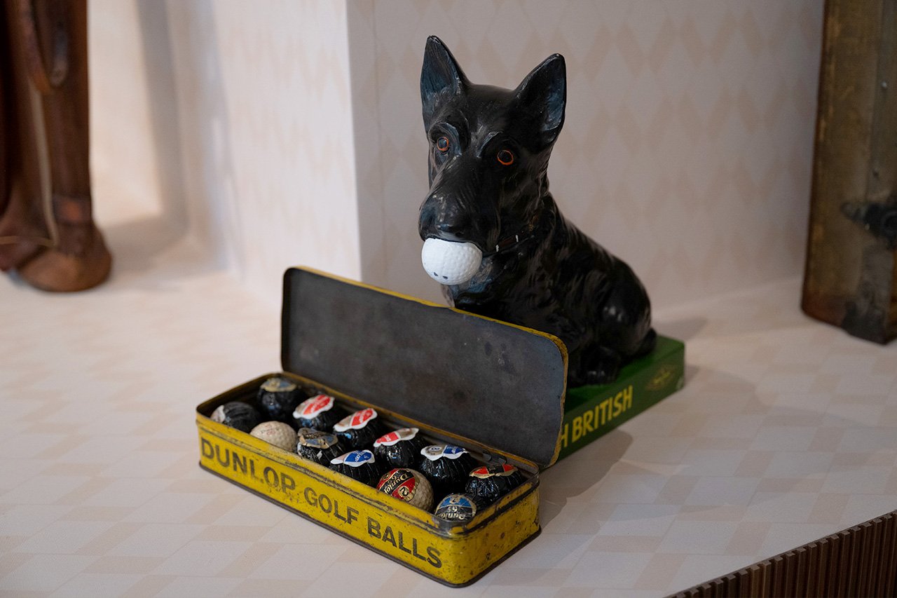 A vintage black dog figurine holding a golf ball beside an open Dunlop golf ball tin.