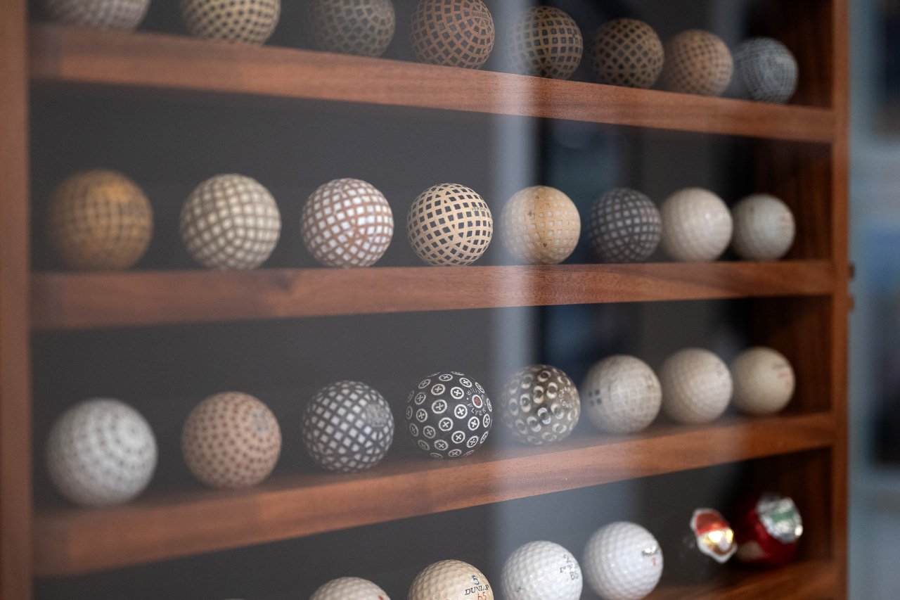 A collection of vintage golf balls displayed on wooden shelves behind glass.