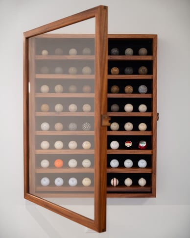 An open wooden display cabinet containing a collection of historic golf balls.