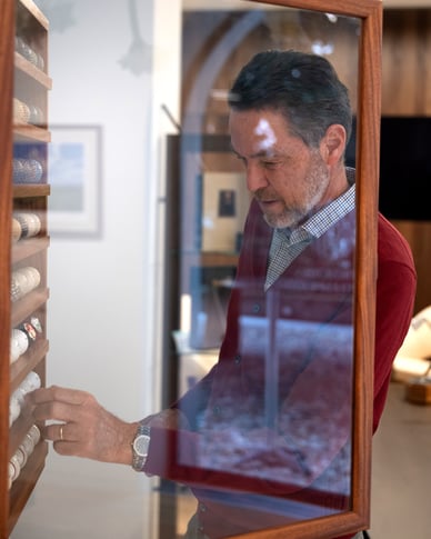 Paolo Quirici examining a collection of historic golf balls inside a wooden display cabinet.