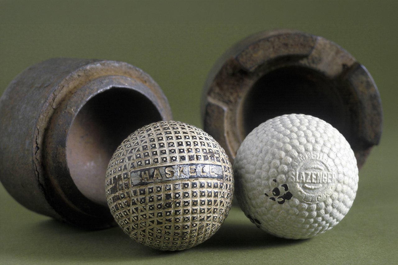 Vintage Haskell and Slazenger golf balls displayed beside two antique ball moulds.