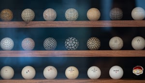 A collection of vintage golf balls from different eras displayed on wooden shelves.