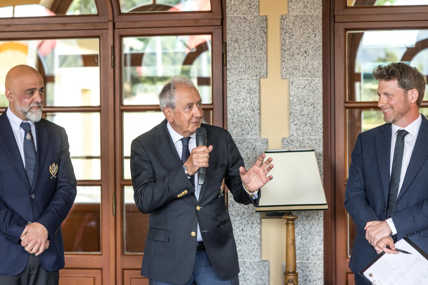 Speaker addressing guests during the prize-giving ceremony of the Hickory Masters at Villa d’Este Golf Club, with officials standing alongside in the clubhouse setting.