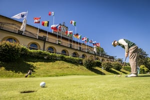 Hickory golfer putting on the practice green in front of the historic clubhouse at Villa d’Este Golf Club, with international flags flying during the Hickory Masters 2026.