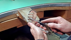 Craftsperson engraving a metal trophy shaped like a vintage hickory golf club head at a jeweller’s workbench using a hand file.