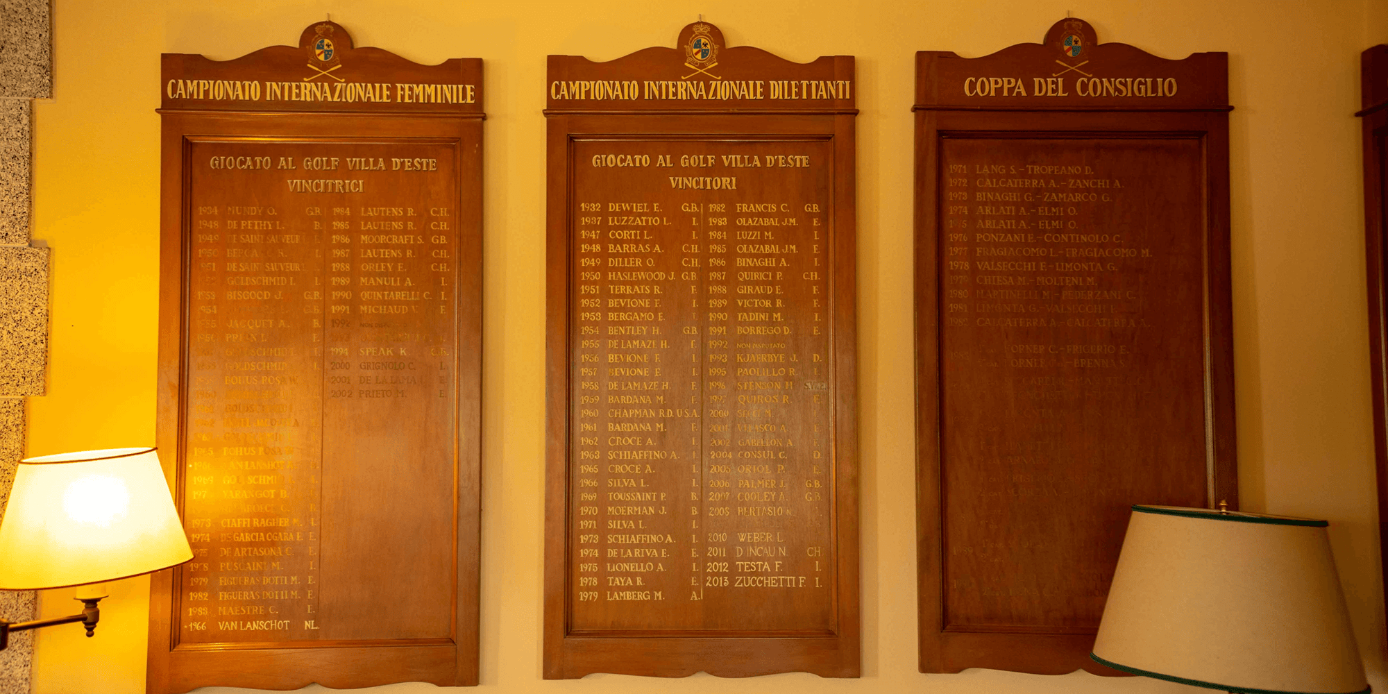 Wooden honor boards displayed on a wall at Golf Villa d’Este, listing past winners of the “Campionato Internazionale Femminile,” “Campionato Internazionale Dilettanti,” and “Coppa del Consiglio.” The names, nationalities, and years of the champions are engraved in gold lettering