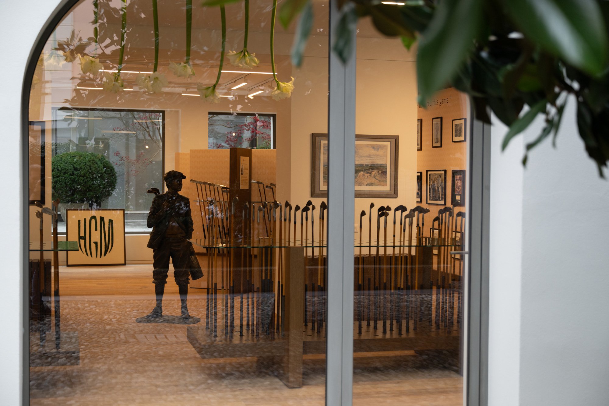 Exterior view through a window into the Hickory Golf Masters Museum, showing vintage golf clubs, artwork, and a bronze statue.